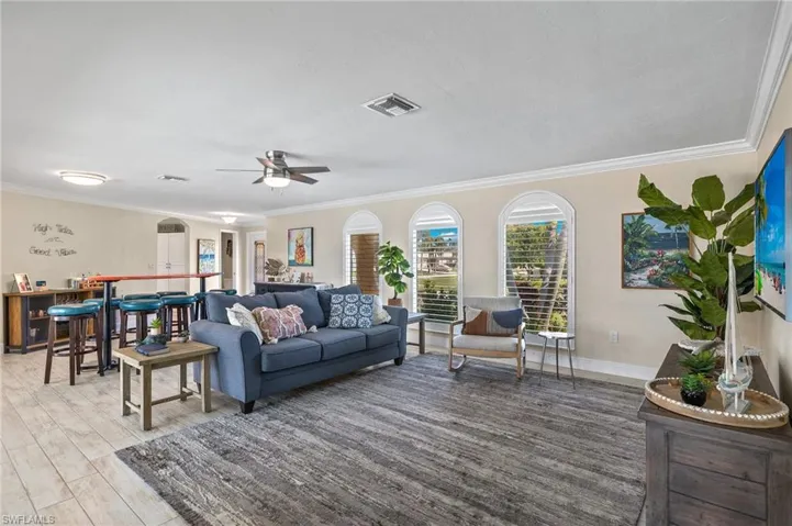 Living room featuring crown molding, light wood-style floors, a ceiling fan, and arched walkways