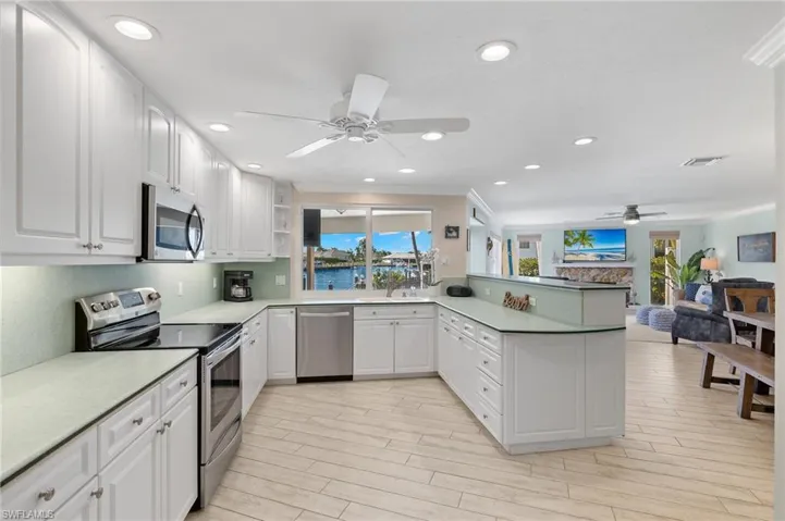 Kitchen with stainless steel appliances, white cabinets, a peninsula, open floor plan, and a ceiling fan