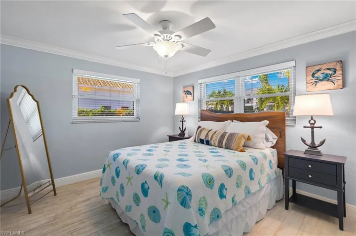 Bedroom with light wood finished floors, ornamental molding, and a ceiling fan
