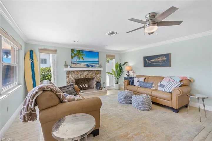 Living room featuring a stone fireplace, crown molding, wood finished floors, and ceiling fan