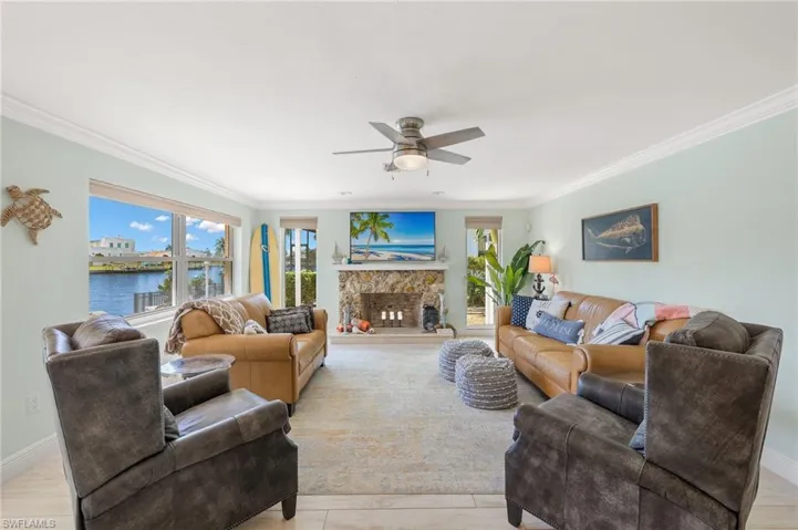 Living area featuring a ceiling fan, crown molding, a fireplace, healthy amount of natural light, and light wood-style flooring