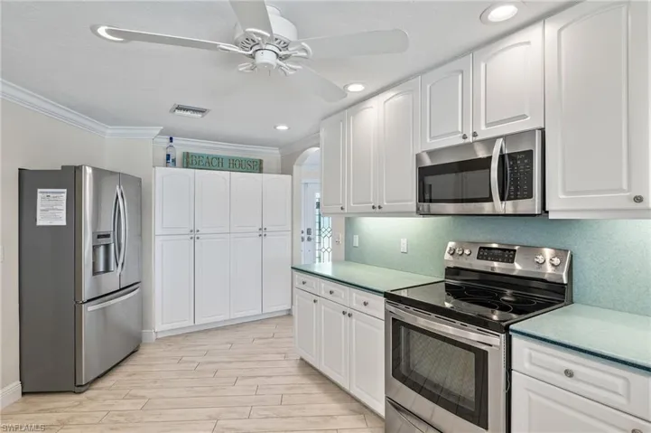 Kitchen with stainless steel appliances, crown molding, white cabinetry, recessed lighting, and ceiling fan