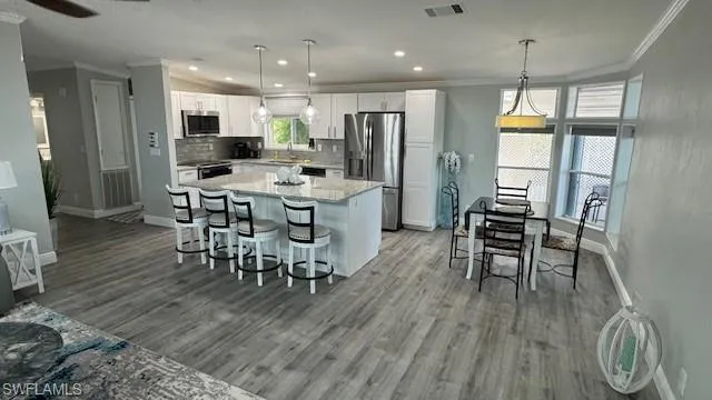 Open concept:  Kitchen with large island, granite countertops, white cabinetry, commercial grade flooring, appliances with stainless steel finishes, and backsplash