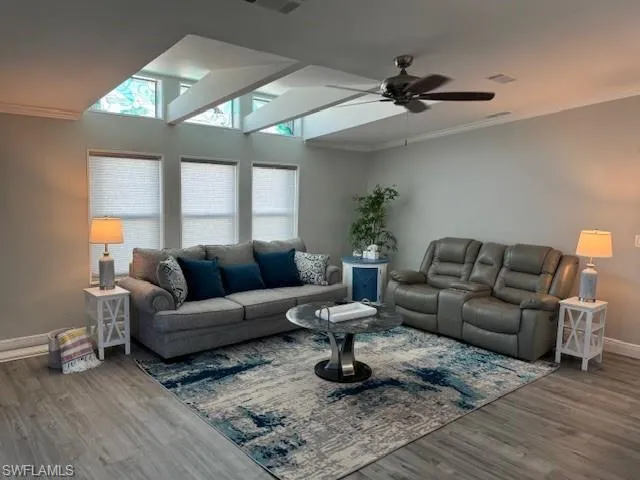 Living room with vaulted ceilling, decorative stained glass, ornamental molding, and ceiling fan