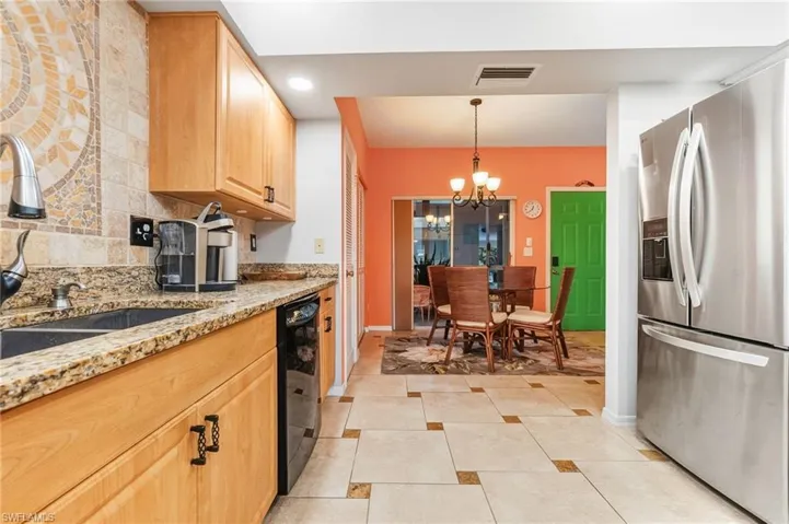 Kitchen featuring stainless steel fridge with ice dispenser, light stone counters, a chandelier, light brown cabinets, and hanging light fixtures