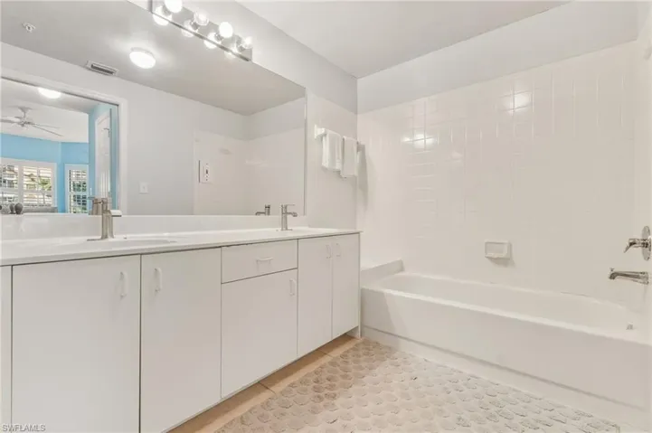 Full bathroom featuring double vanity, light tile patterned flooring, bathing tub / shower combination, and a ceiling fan