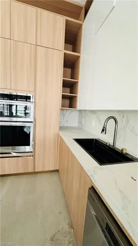 Kitchen featuring modern cabinets, light wood finish cabinets, stainless steel appliances, light stone countertops, and open shelves