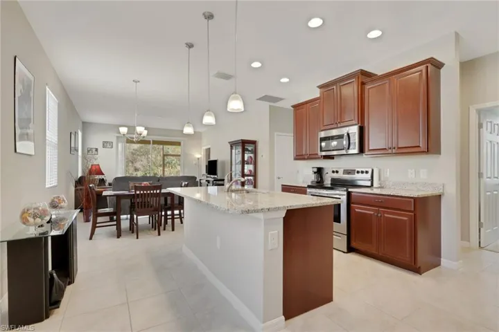 Kitchen with appliances with stainless steel finishes, light stone counters, decorative light fixtures, recessed lighting, and a center island with sink