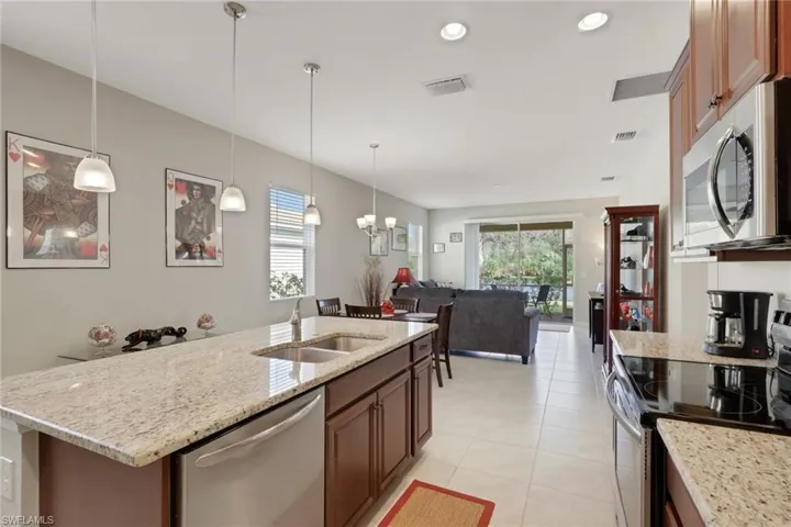 Kitchen with stainless steel appliances, light stone counters, pendant lighting, a kitchen island with sink, and recessed lighting