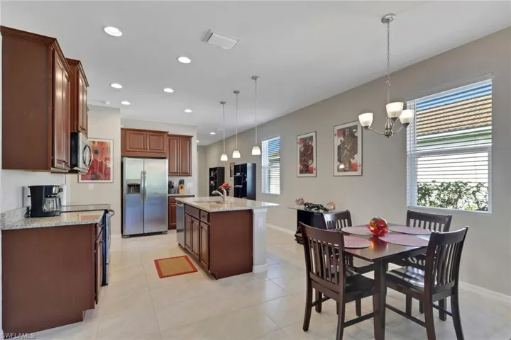 Kitchen featuring light stone countertops, appliances with stainless steel finishes, recessed lighting, decorative light fixtures, and a center island with sink