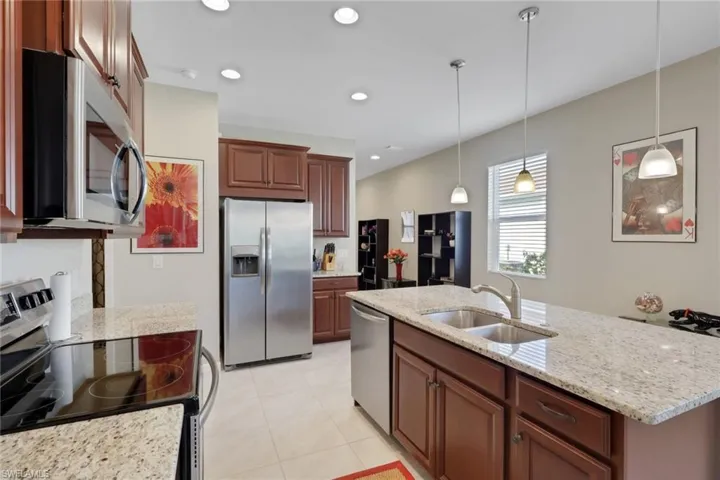 Kitchen with appliances with stainless steel finishes, recessed lighting, pendant lighting, light stone countertops, and an island with sink