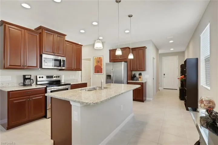Kitchen with appliances with stainless steel finishes, light tile patterned floors, decorative light fixtures, an island with sink, and recessed lighting