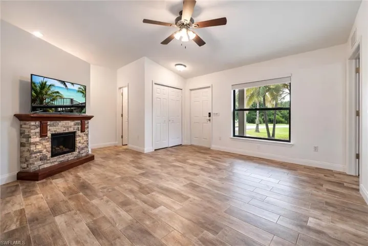 Unfurnished living room with a stone fireplace, ceiling fan, light wood-type flooring, and vaulted ceiling