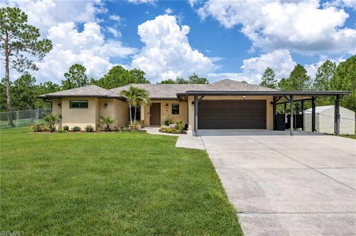 View of front of property with stucco siding, a garage, driveway, a storage unit, and roof with shingles