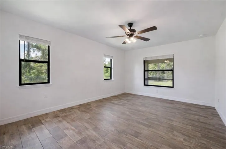 Unfurnished room with dark wood-type flooring, plenty of natural light, and a ceiling fan