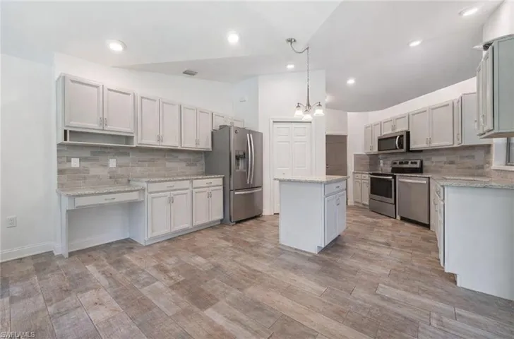 Kitchen featuring lofted ceiling, stainless steel appliances, a center island, suspended lighting, and light stone counters