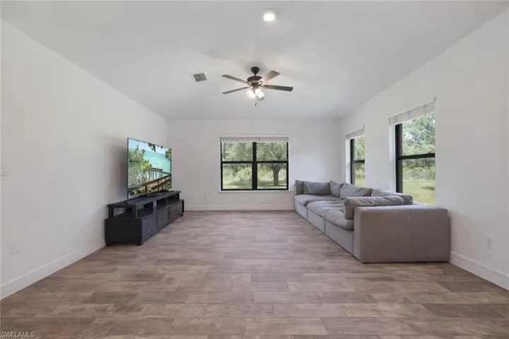 Living room with light wood-style flooring, a ceiling fan, and healthy amount of natural light