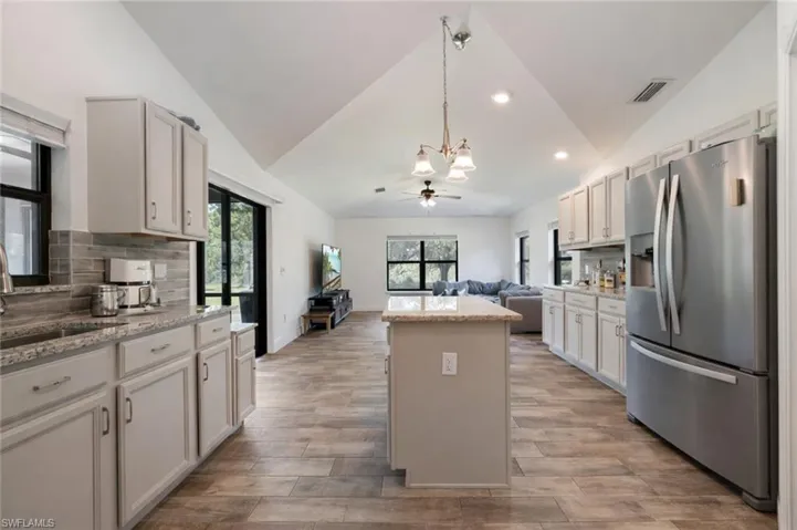 Kitchen with decorative backsplash, open floor plan, stainless steel fridge, lofted ceiling, and a center island