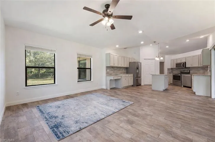 Kitchen featuring open floor plan, a kitchen island, a ceiling fan, backsplash, and stainless steel appliances