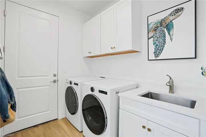 Clothes washing area featuring light wood-type flooring, cabinet space, separate washer and dryer, and a sink