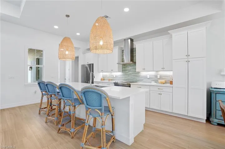 Kitchen featuring a center island with sink, a breakfast bar, stainless steel appliances, wall chimney range hood, and a sink