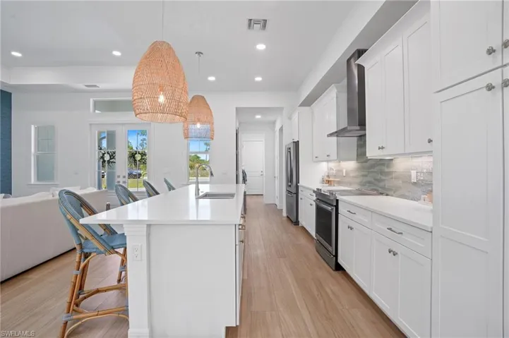 Kitchen featuring stainless steel appliances, a sink, visible vents, open floor plan, and wall chimney range hood