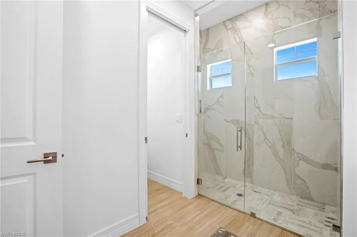 Full bath with a marble finish shower, baseboards, and wood finished floors