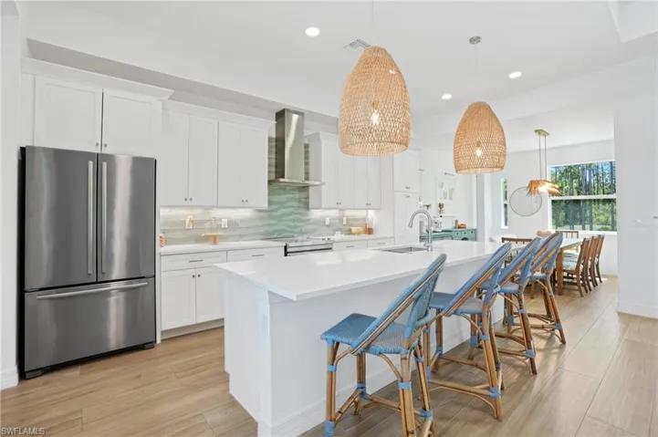 Kitchen with stainless steel appliances, white cabinets, wall chimney range hood, backsplash, and a center island with sink