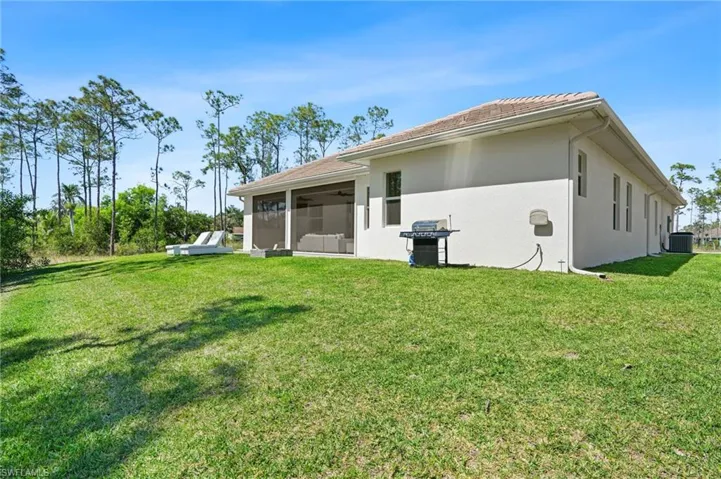 Rear view of house with central AC, a lawn, a sunroom, and stucco siding