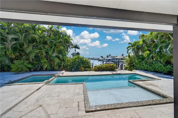 The property features a pool and spa, surrounded by a tiled patio, with lush tropical foliage, and a canal view