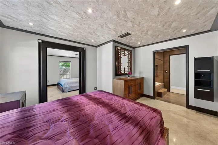 A bedroom featuring a textured ceiling with recessed lighting, an open doorway leading to a bathroom with a tub, and a wooden dresser with a decorative mirror