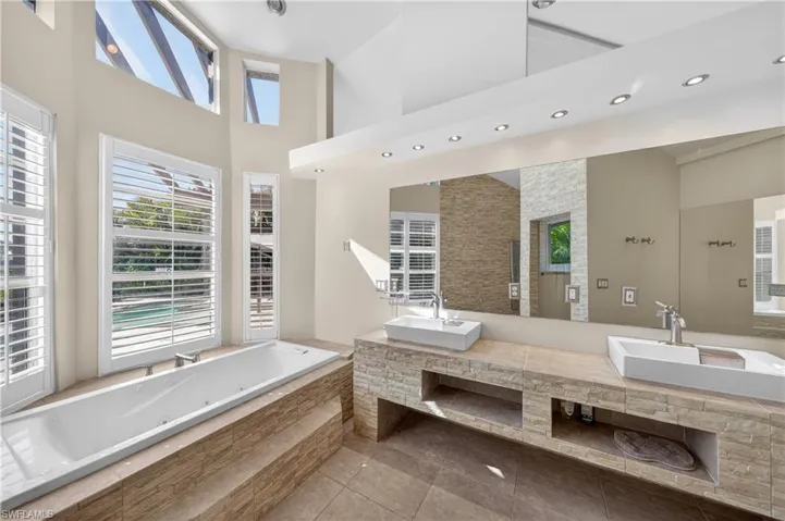 This bathroom features a large soaking tub, dual vanity with vessel sinks, and ample natural light from the large windows with white shutters