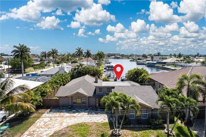 The property features a large home with a paved driveway, surrounded by lush landscaping and palm trees