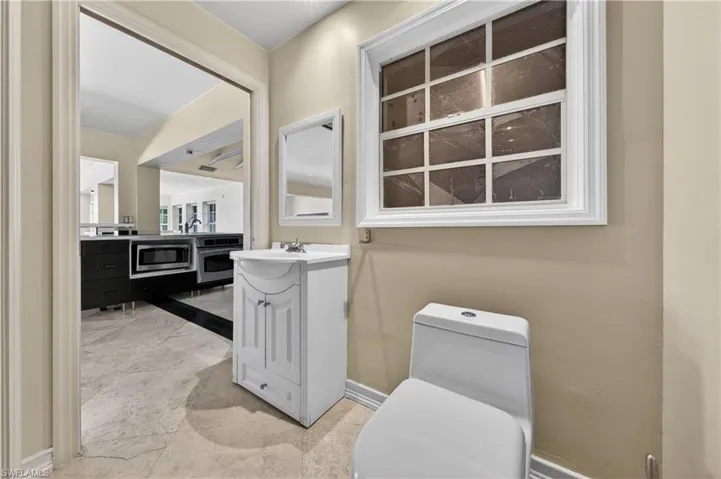 This powder room features a white vanity with a rectangular sink, a toilet, and a window with white trim