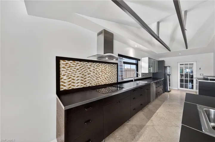 The kitchen features dark cabinetry, integrated appliances, and a mosaic tile backsplash