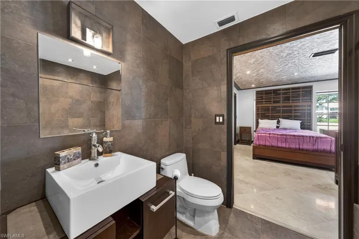 Bathroom featuring a rectangular vessel sink with a modern faucet, a toilet, and dark-toned wall tiles