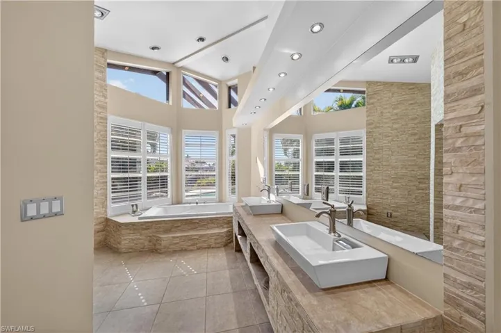 Spacious bathroom featuring dual vessel sinks, a large mirror, and a built-in bathtub with surrounding windows
