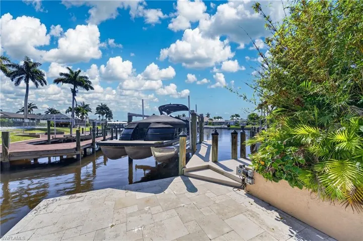 Waterfront property featuring a private dock with a boat lift, stone paver patio, and lush landscaping