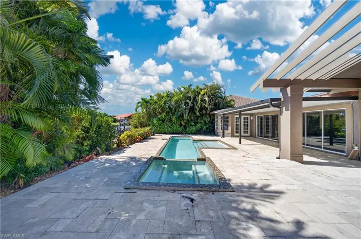 The property features an expansive outdoor patio with a swimming pool, integrated spa, and a pergola, all set against a backdrop of lush tropical foliage