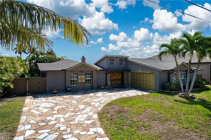 This property features a stone driveway, a well-maintained lawn, and mature palm trees