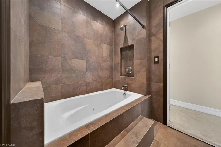 The bathroom features a built-in tub with jets, a tiled surround, a built-in shower niche, and a rain showerhead
