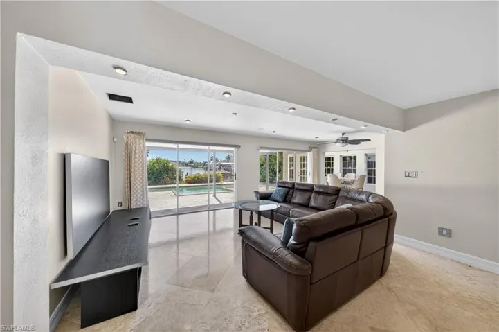 Spacious living area featuring polished tile flooring, recessed lighting, and large sliding glass doors that provide views of the pool and waterway
