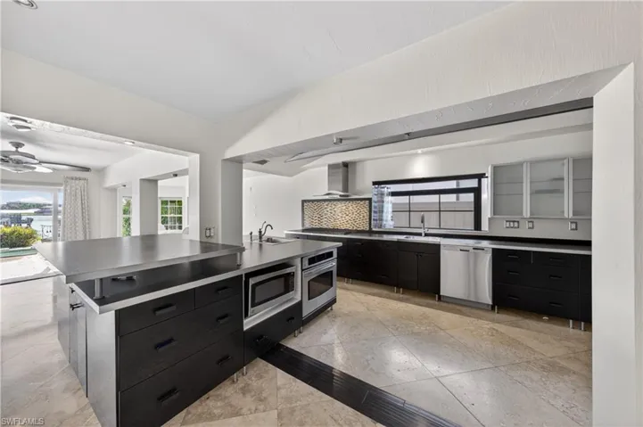 The kitchen features an expansive island with an integrated microwave and oven, dark cabinetry, and light-colored tile flooring