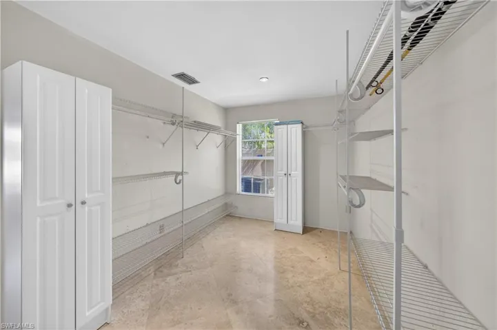 This spacious walk-in closet features ample shelving, a window, and two white storage cabinets