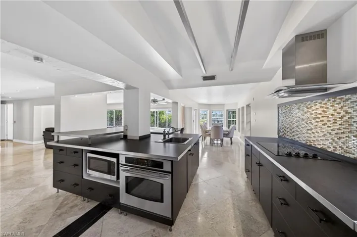 The kitchen features dark cabinetry, stainless steel appliances, a cooktop, and a mosaic tile backsplash