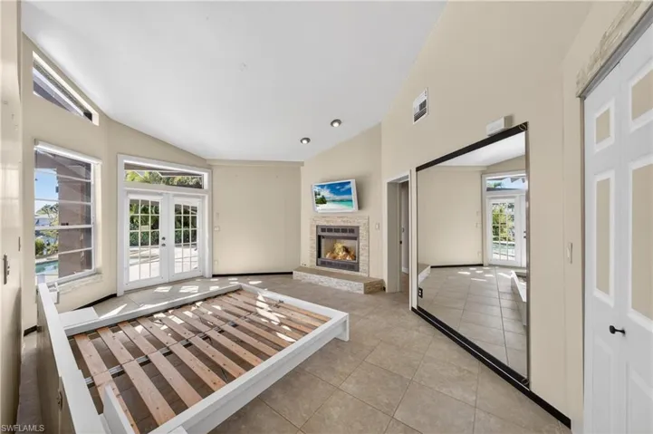 This spacious room features vaulted ceilings, tile flooring, a fireplace with a stone hearth, and double French doors opening to an exterior patio