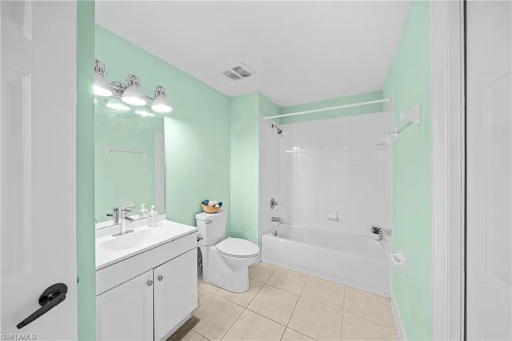 Full bathroom featuring tile patterned flooring, vanity, tiled shower / bath combo, and toilet
