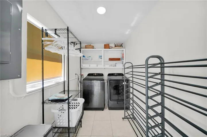 Laundry area featuring electric panel, light tile patterned flooring, and washer and clothes dryer