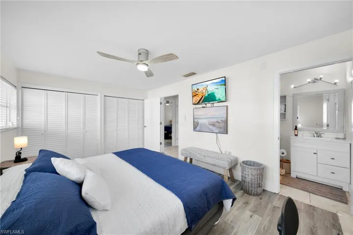 Bedroom with two closets, light wood-type flooring, ceiling fan, and connected bathroom