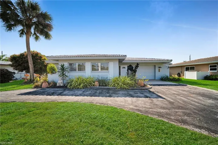 Ranch-style home featuring driveway, a tile roof, a front yard, and an attached garage